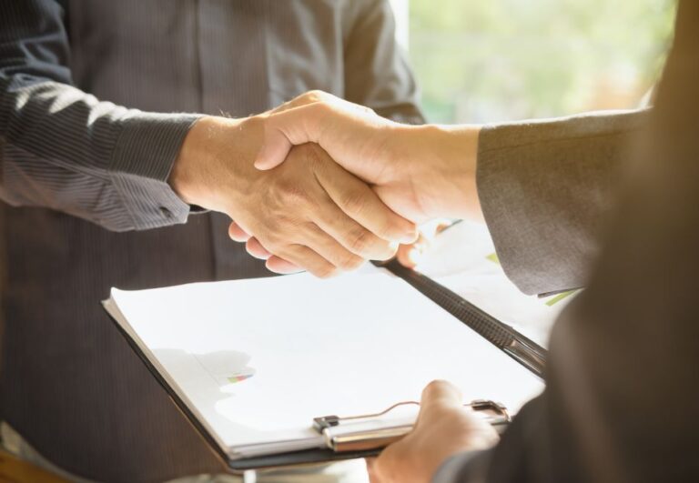 Dwie osoby podają sobie ręce nad dokumentami związanymi z dofinansowaniem inwestycji GOZ z KPO