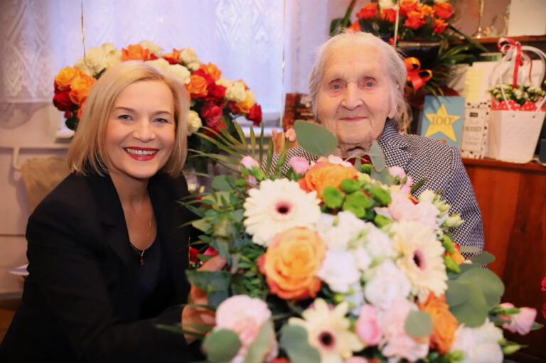 Stulatka z kwiatami w towarzystwie uśmiechniętej kobiety