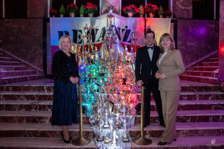 Uczestnicy Gali Jubileuszowej Zespołu Rewanż stojący przed stołem pełnym trofeów