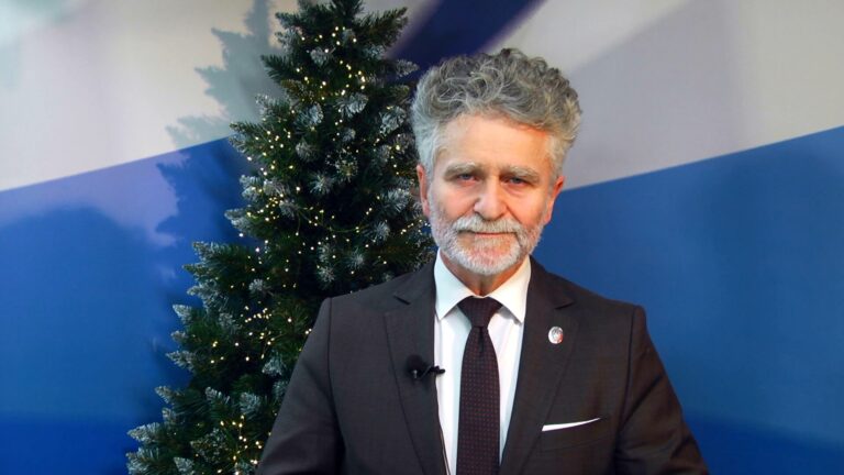 Senator RP składa życzenia bożonarodzeniowe przy choince z lampkami