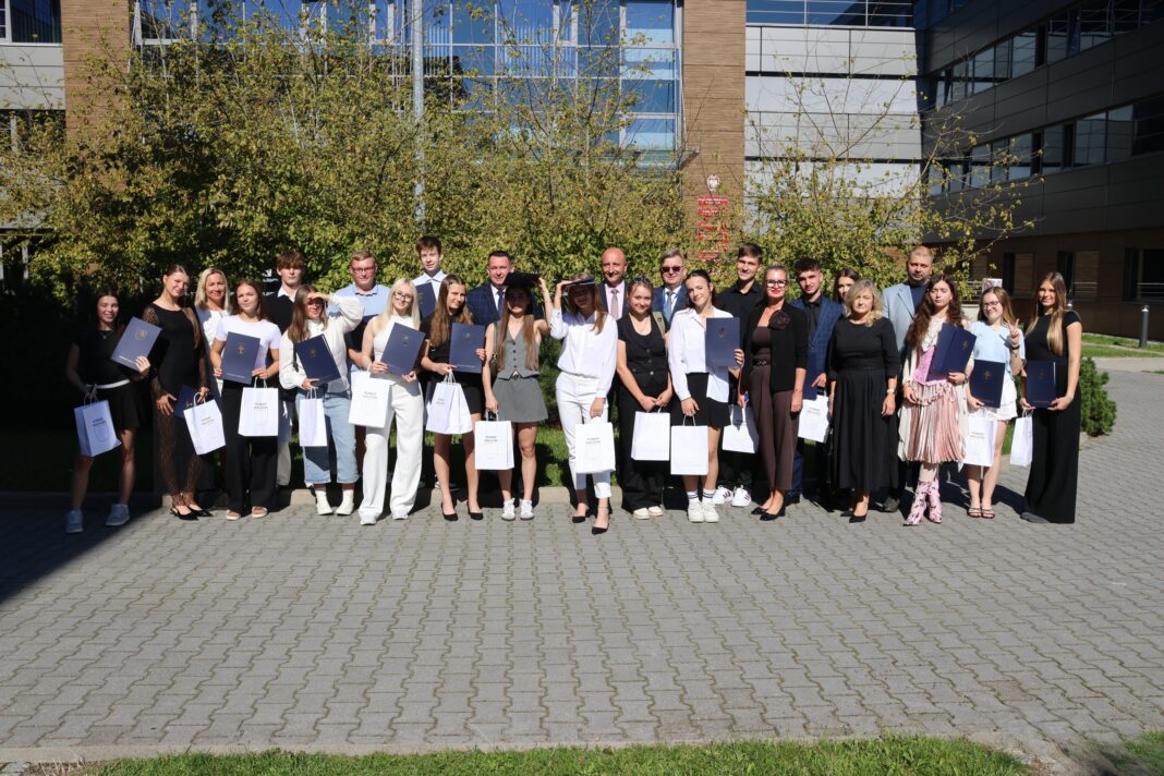 Grupa osób, laureaci stypendium, stoją razem z dyplomami przed budynkiem.