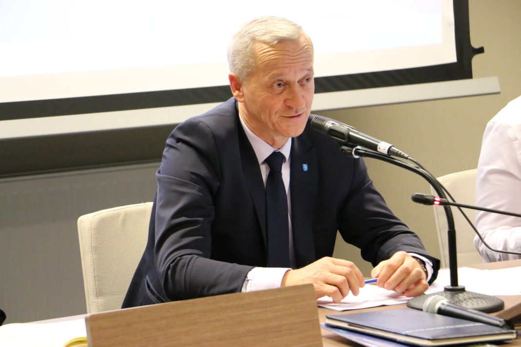 Mężczyzna w garniturze prowadzi sesję Rady Powiatu.