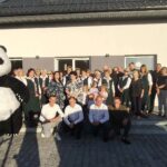 Grupa osób pozująca na tle budynku z maskotką pandy