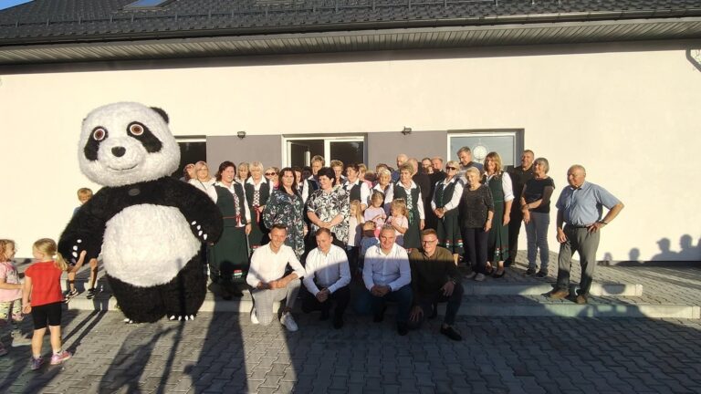 Grupa osób pozująca na tle budynku z maskotką pandy