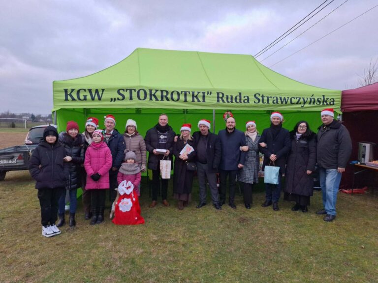 Grupa ludzi przed namiotem KGW Stokrotki Ruda Strawczyńska podczas wydarzenia świątecznego