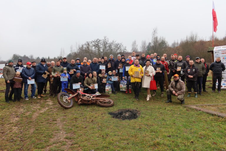 Grupowe zdjęcie osób związanych z KTM Novi Kielce, stojących na tle motocykla terenowego.
