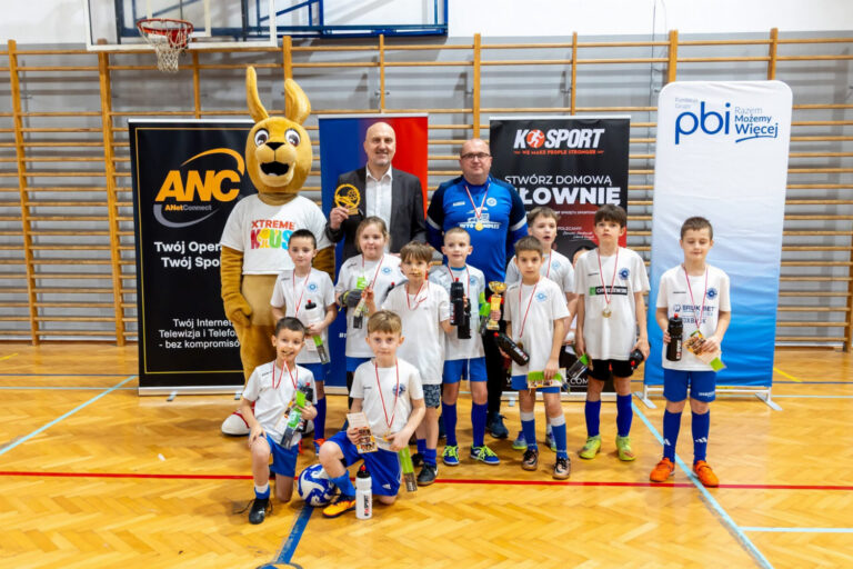 Grupa dzieci i dorosłych z maskotką podczas Turnieju Piłkarskie Skarby & Family Cup