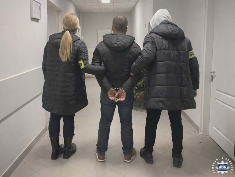 Policjanci prowadzą osobę w kajdankach korytarzem budynku