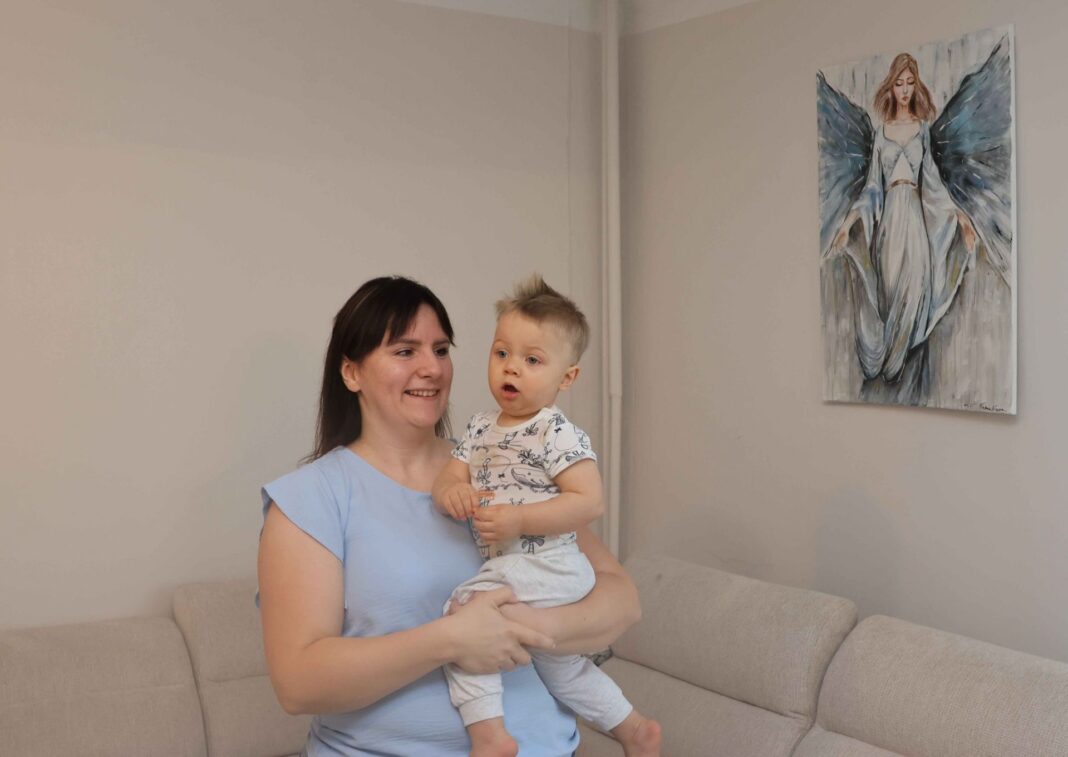 Kobieta trzymająca dziecko w salonie z obrazem anioła na ścianie