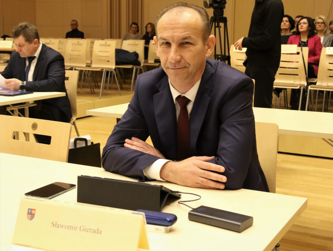 Mężczyzna w garniturze siedzący przy stole z tabliczką z nazwiskiem na posiedzeniu komisji w Świętokrzyskim