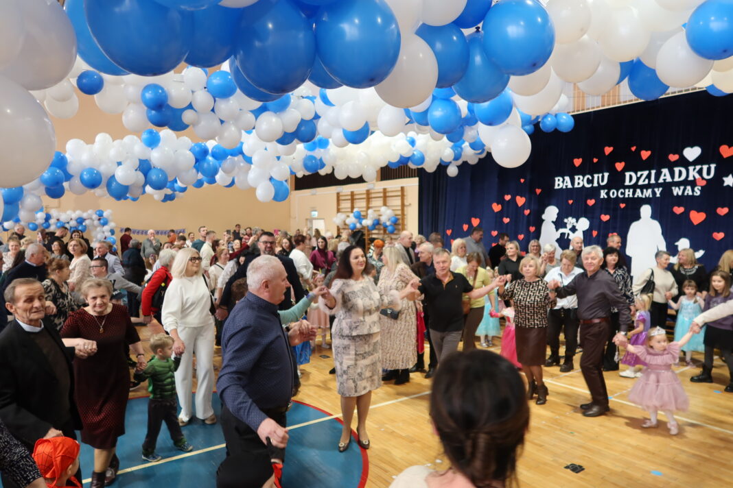 Ludzie tańczą na Międzypokoleniowym Balu Babci i Dziadka w Piekoszowie pod dekoracjami z balonów.