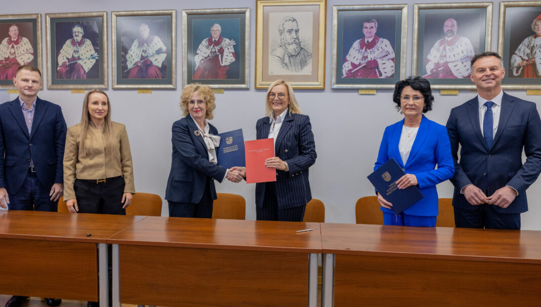 Grupa osób podczas podpisywania umowy w sali z portretami na ścianie