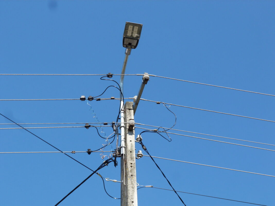 Słup elektryczny z lampą uliczną na tle błękitnego nieba.