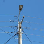 Słup elektryczny z lampą uliczną na tle błękitnego nieba.