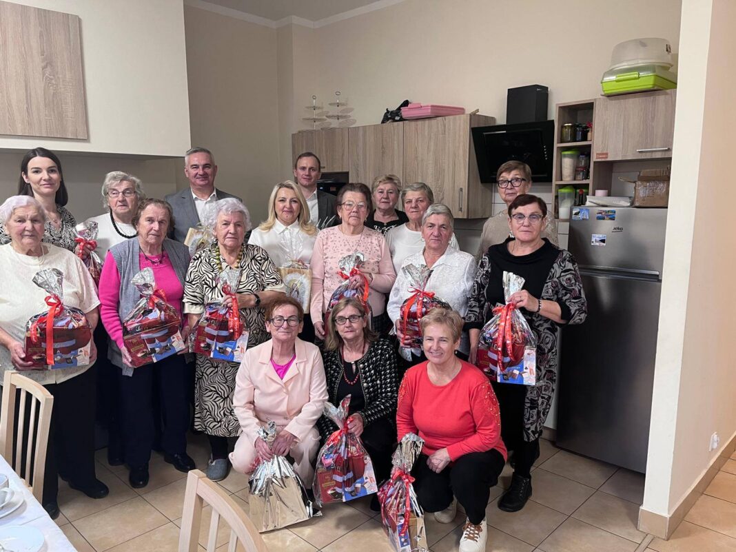 Grupa seniorów i opiekunów podczas spotkania w Klubie Seniora w Mniowie, trzymających upominki.