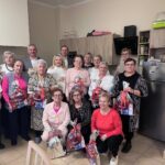 Grupa seniorów i opiekunów podczas spotkania w Klubie Seniora w Mniowie, trzymających upominki.
