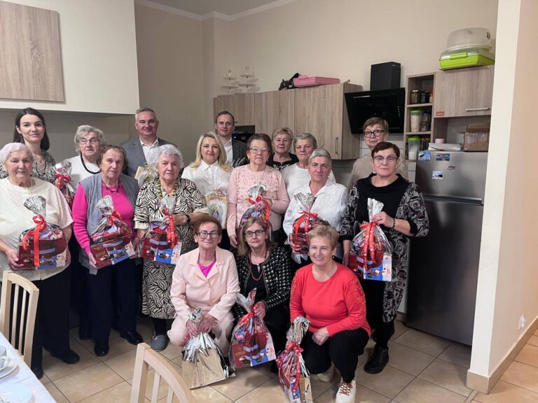 Grupa seniorów i opiekunów podczas spotkania w Klubie Seniora w Mniowie, trzymających upominki.