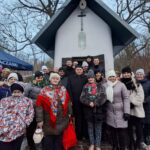 Grupa osób stojąca przed kapliczką podczas wydarzenia kolędowego w Kuźniakach.