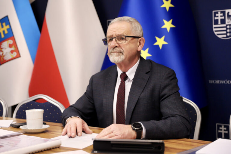 Mężczyzna w garniturze siedzący przy stole na tle flag