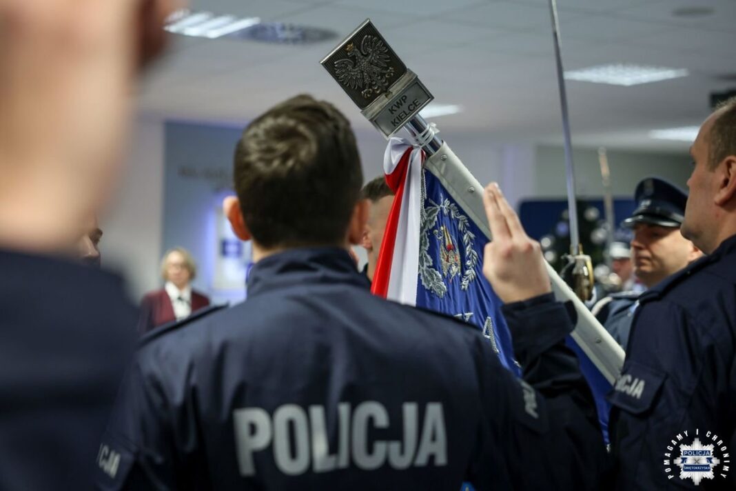 Grupa polskich policjantów podczas ceremonii ślubowania, trzymających sztandar z godłem i napisem KWP Kielce.