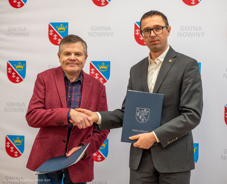 Dwie osoby ściskające dłonie na tle logo Gmina Nowiny, trzymające teczki z dokumentami.