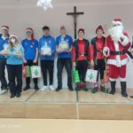 Grupa młodych ludzi w świątecznych strojach na scenie podczas wizyty w Domu Pomocy Społecznej.