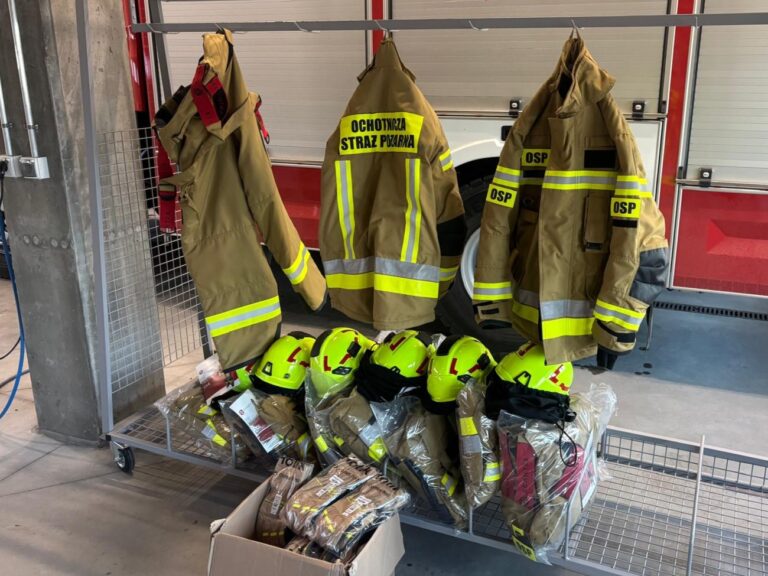 Nowe ubrania bojowe i kaski dla Ochotniczej Straży Pożarnej z Bilczy, leżące na wózku w remizie strażackiej.
