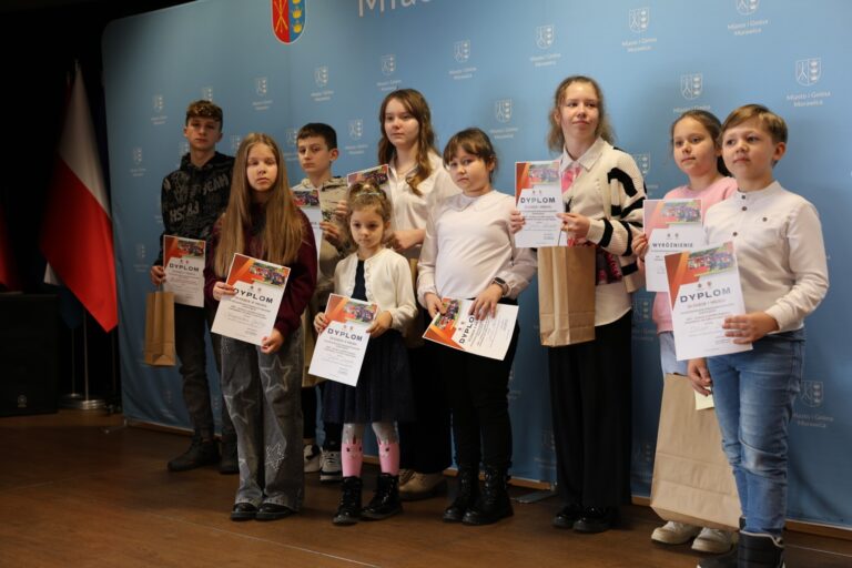 Grupa dzieci z dyplomami na tle ścianki z herbami i flagami podczas Ogólnopolskiego Strażackiego Konkursu Plastycznego