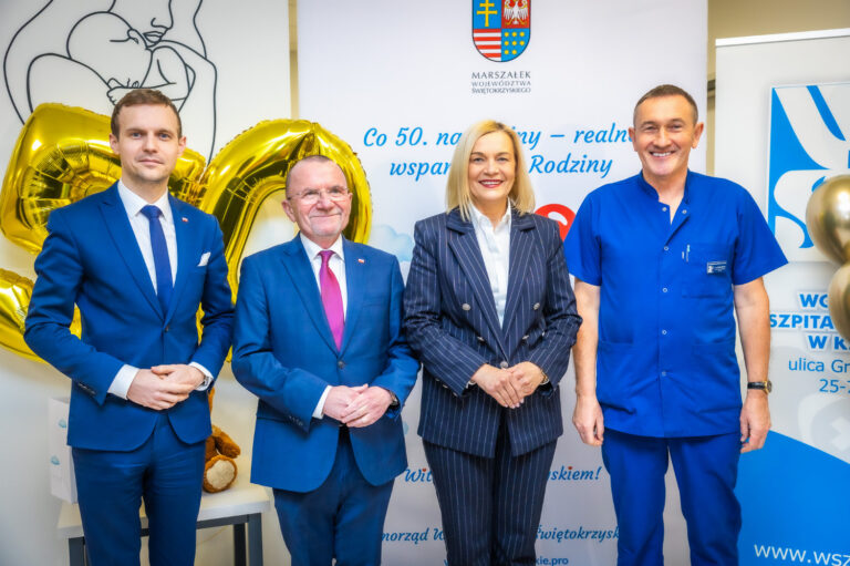 Grupa osób na tle balonów i plakatu programu wsparcia dla rodzin