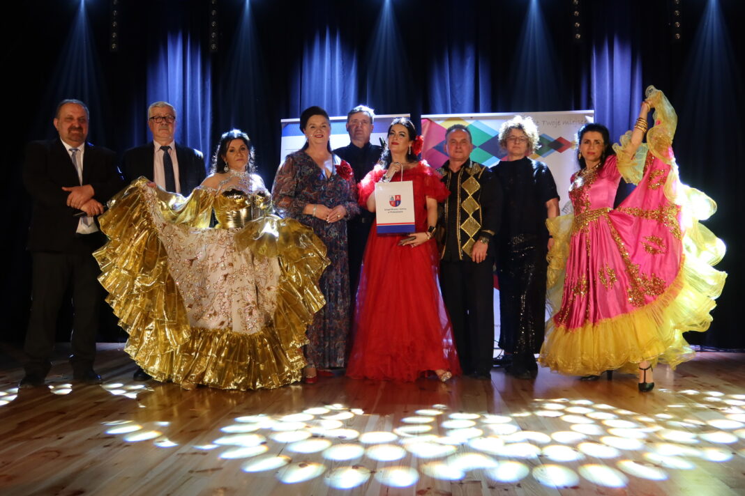 Grupa osób na scenie w strojach cygańskich podczas wydarzenia w Piekoszowie.