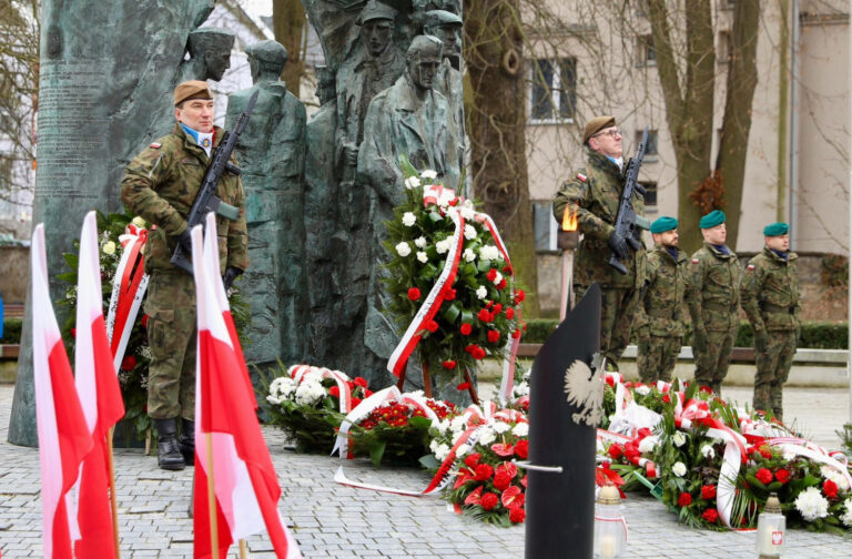 Żołnierze na uroczystości przy pomniku Armii Krajowej z wieńcami i flagami Polski