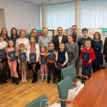 Grupa młodych artystów z Nowin wraz z opiekunami, trzymających nagrody za udział w konkursie plastycznym.