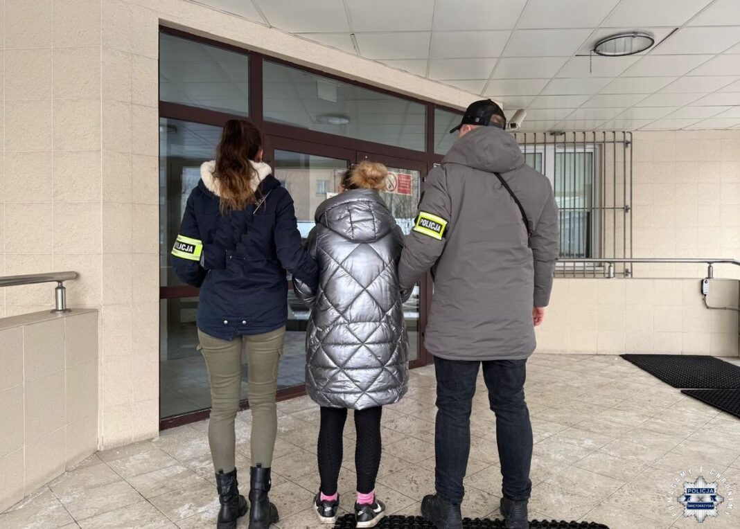 Policjanci prowadzą osobę aresztowaną do budynku