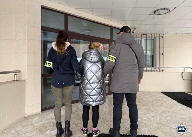 Policjanci prowadzą osobę aresztowaną do budynku