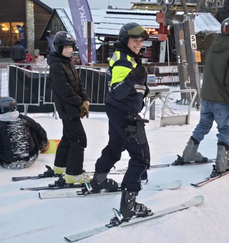 Grupa narciarzy, w tym policjant w mundurze, na stoku narciarskim.