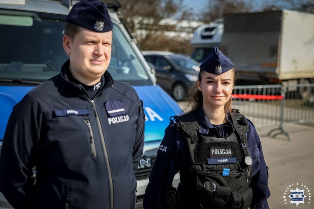 Dwóch policjantów, kobieta i mężczyzna, stoją przed radiowozem